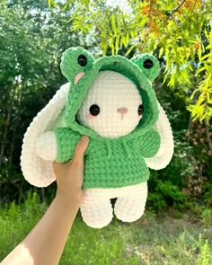 a person holding up a crocheted stuffed animal in front of some trees and bushes