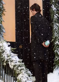 a man standing in front of a black door with snow falling on the ground and trees