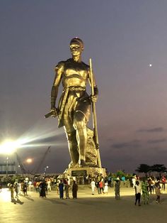 a large golden statue is in the middle of a plaza with people standing around it