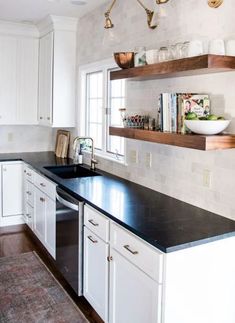 a kitchen with white cabinets and black counter tops in front of open shelves above the sink