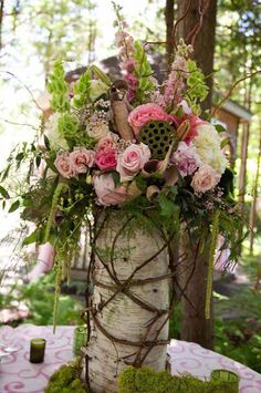 a vase filled with flowers and greenery sitting on top of a white table cloth