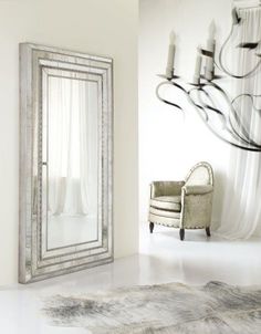 a mirror sitting on top of a white floor next to a chair and chandelier