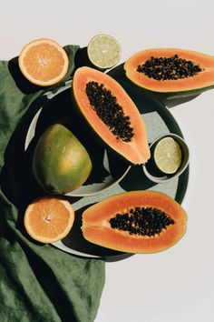 papaya, limes and kiwi are arranged on a green plate with two spoons