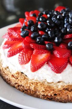 a cake with strawberries and blueberries on top sitting on a white platter