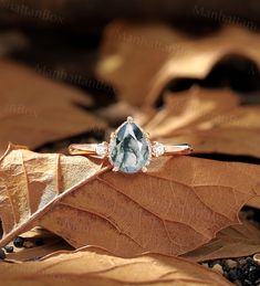 an aquamarine colored diamond ring sitting on top of a leaf in the sun with other leaves surrounding it