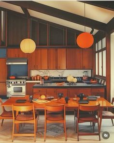 an image of a kitchen setting with table and chairs in the center, lights hanging from the ceiling