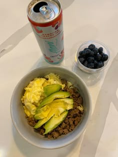 a white bowl filled with food next to a can of soda and some blueberries