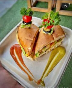 a sandwich cut in half on top of a plate with pickles and tomato slices