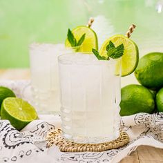 two glasses filled with lemonade and limes on a table next to some limes