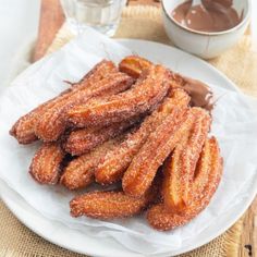 some churros are on a white plate with dipping sauce in the back ground