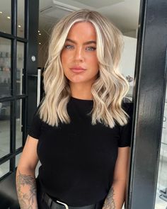 a woman with blonde hair and tattoos standing in front of a glass door looking at the camera