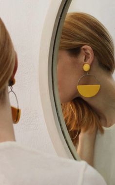 a woman is looking at her reflection in the mirror while wearing yellow earrings