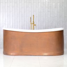 an old fashioned bathtub in a bathroom with white tile walls and floor, along with a gold faucet