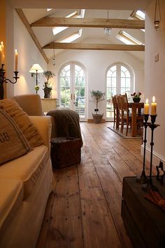 a living room filled with furniture and lots of windows next to a wooden floor covered in candles