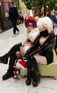 two women dressed in costumes sitting on a bench at a shopping mall, one wearing black boots and the other with white hair