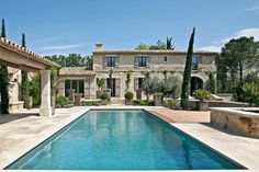 an outdoor swimming pool surrounded by stone walls and pillars, with trees in the background