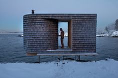 a person standing in the doorway of a building on top of snow covered ground next to water