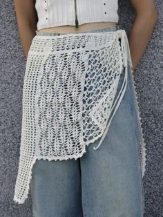 a woman is standing in front of a wall wearing a white crochet skirt