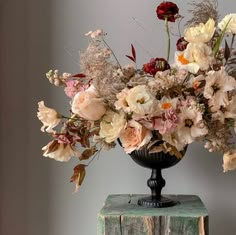 a vase filled with lots of flowers sitting on top of a wooden table next to a wall