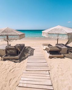 lounge chairs and umbrellas on the beach with clear blue water in the back ground