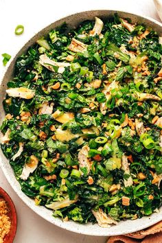 a white bowl filled with greens and nuts on top of a table next to a wooden spoon