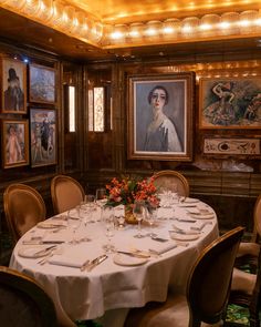 a dining room table set with place settings for four people and paintings on the wall behind it