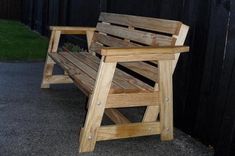 a wooden bench sitting in front of a black fence with grass on the other side