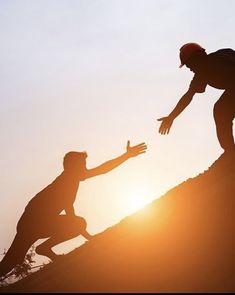 two people on top of a hill with the sun setting behind them and one person reaching out