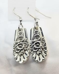 pair of silver earrings with ornate design on them, sitting on a white cloth background