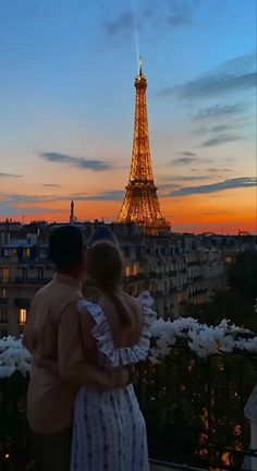 a man and woman standing in front of the eiffel tower at sunset, with their arms around each other