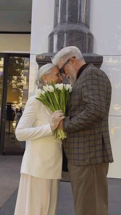 an older man and woman standing next to each other with flowers in front of them