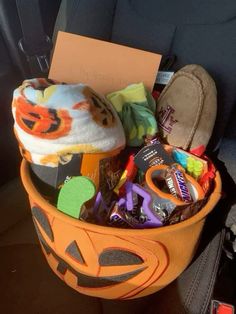 an orange bucket filled with halloween items in the back seat of a car on a sunny day