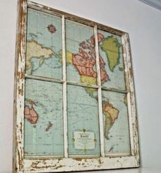 an old window with a world map on the glass in front of it, sitting on a shelf next to a white wall