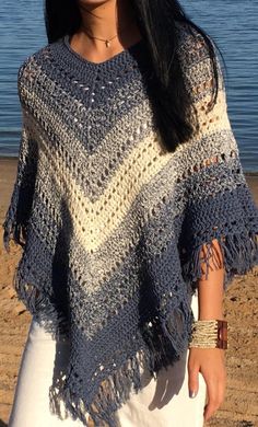 a woman wearing a blue and white crocheted ponchy on the beach