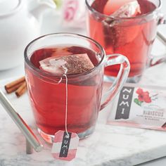 two mugs filled with red tea and ice on a marble counter top next to silverware