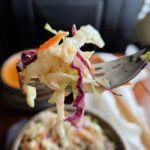 a fork with some food in it on top of a table next to a bowl