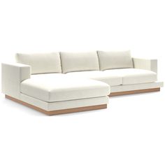 a white sectional couch with wooden legs and pillows on the back, in front of a white background