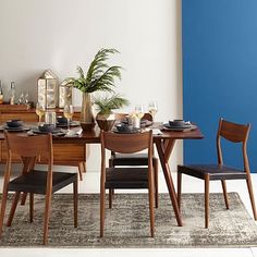 a dining room table set with chairs and plates on it, next to a blue wall