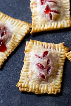 four small pastries with cherries on them sitting on top of a black surface