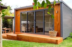 a small wooden deck in front of a house with sliding glass doors and windows on the side