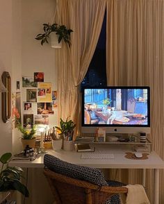 a desk with a computer on it in front of a window filled with pictures and plants