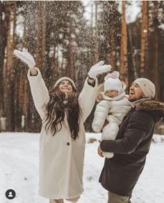 two people standing in the snow with their arms up and one person holding a baby