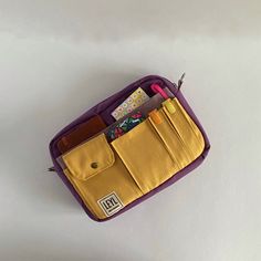 a purple and yellow purse with some pens and pencils in it