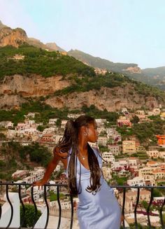 a woman standing on top of a balcony next to a lush green hillside