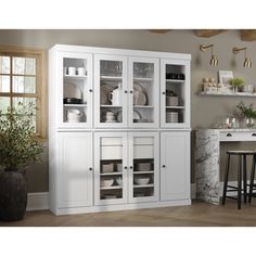 a white china cabinet with glass doors in a living room next to a table and chairs