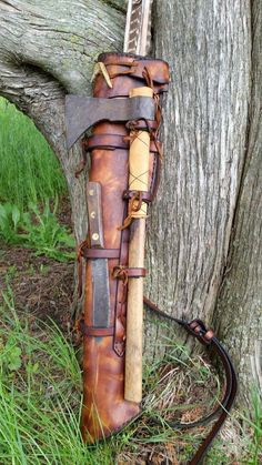 an old leather bag sitting in the grass next to a tree with a long handle