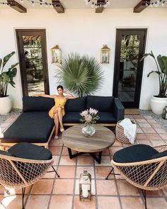 a woman sitting on top of a black couch in a living room next to potted plants