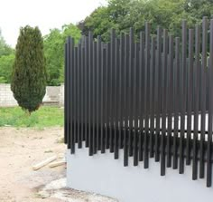 a black metal fence sitting on top of a cement block next to a tree and grass covered field