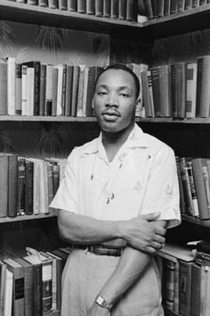 a black and white photo of a man in front of bookshelves with his arms crossed