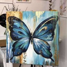 a painting of a blue butterfly with gold accents on it's wings, sitting on a easel